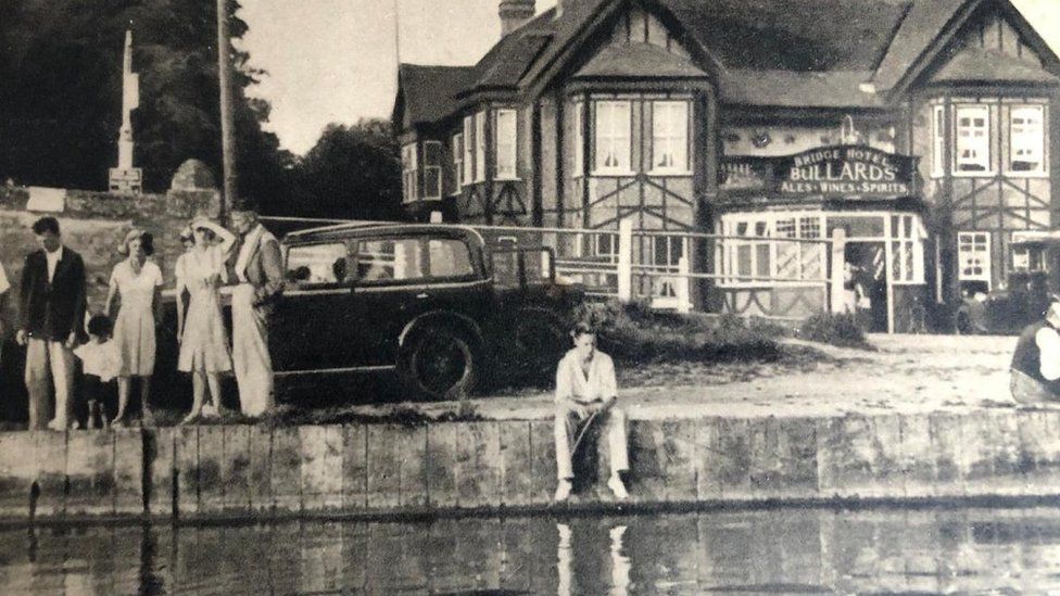 People beside a river, with a pub in the background