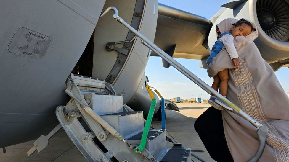 Эвакуированная женщина держит на руках спящего малыша, когда садится в самолет Эмиратов, направляющийся в Абу-Даби, в аэропорту Порт-Судана, 10 мая 2023 г.
