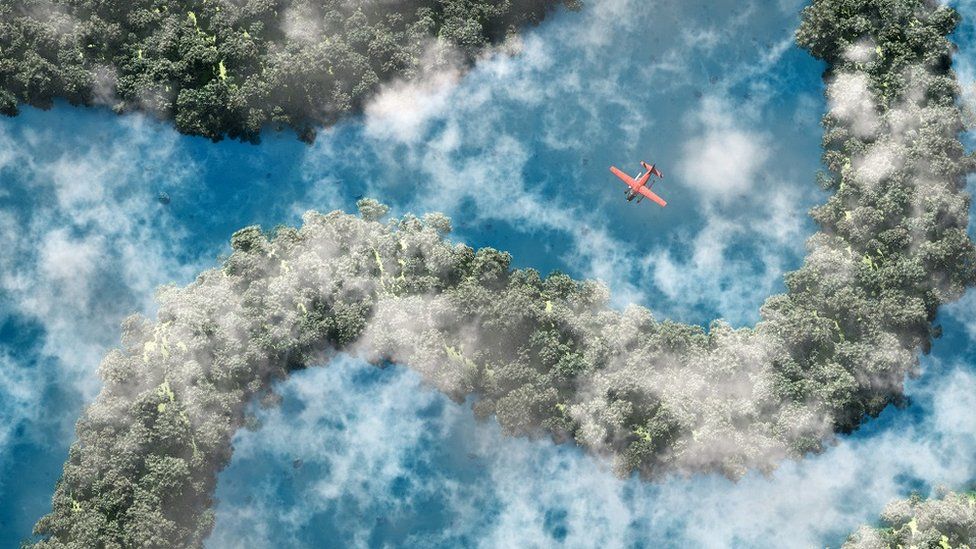 An aerial picture of a red airplane flying over the Amazon rainforest and the river