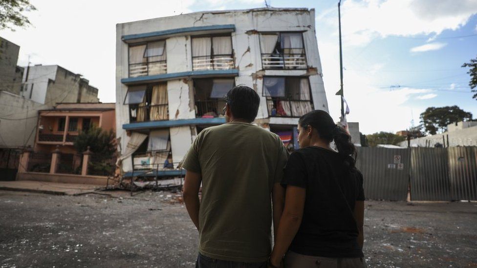 Man and woman stood in front of a damaged building