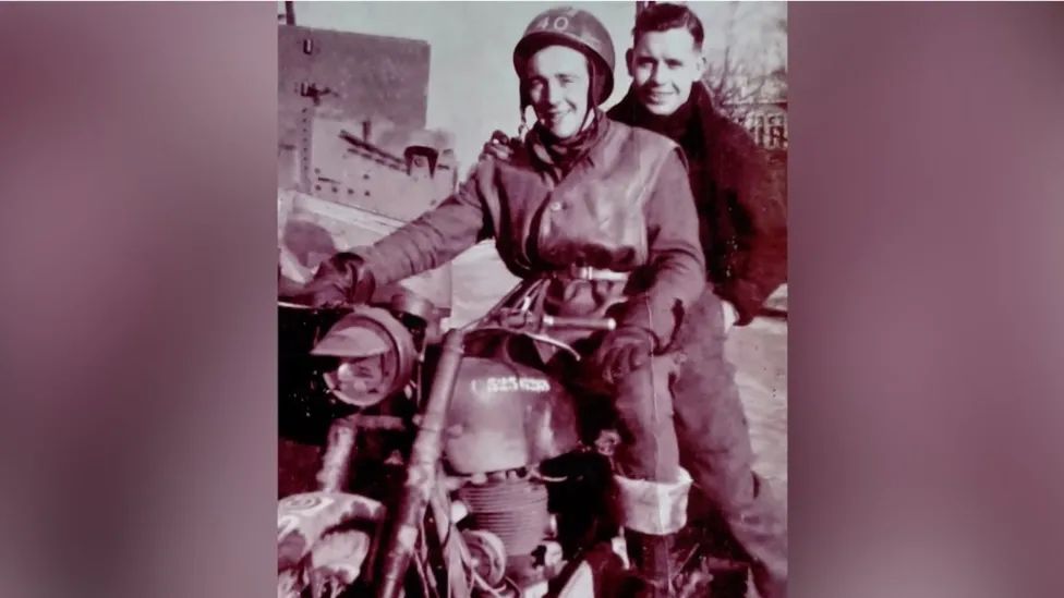 An old black and white photo from World War Two with Don riding a motorbike with a man, both smiling