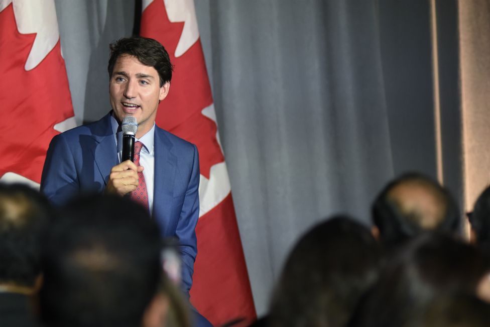 Justin Trudeau speaking at public event in front of Canadian flags