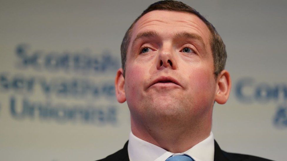Douglas Ross, a close up picture from a lower angle with branding for the Scottish Conservative Party visible behind him