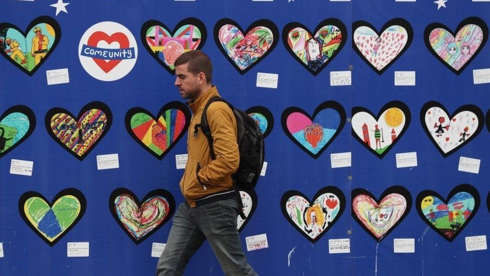 A man walks past an artwork for the victims of the Grenfell Tower fire