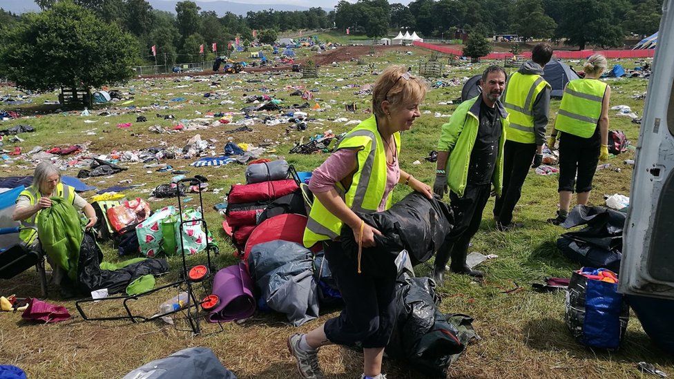 Volunteers collect leftover tents scattered across a field after Kendal Calling