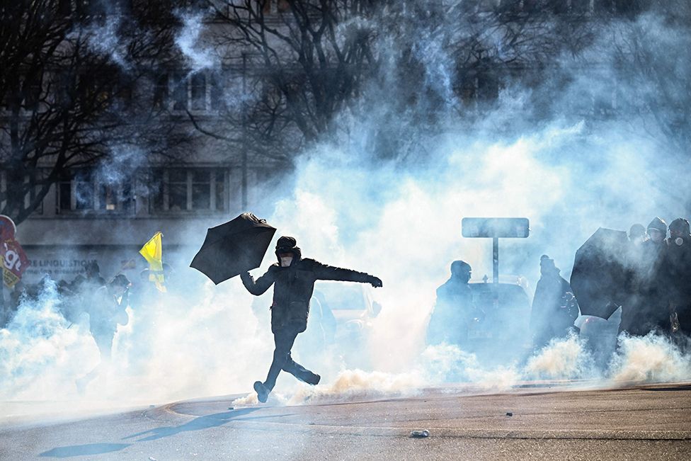A protester with an umbrella kicks away a teargas canister during a demonstration against a deeply unpopular pensions overhaul. Nantes, Western France. 7 February 2023.