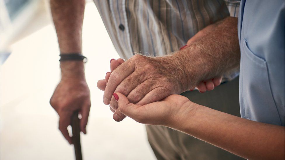 A staff member holds the arm of an elderly man