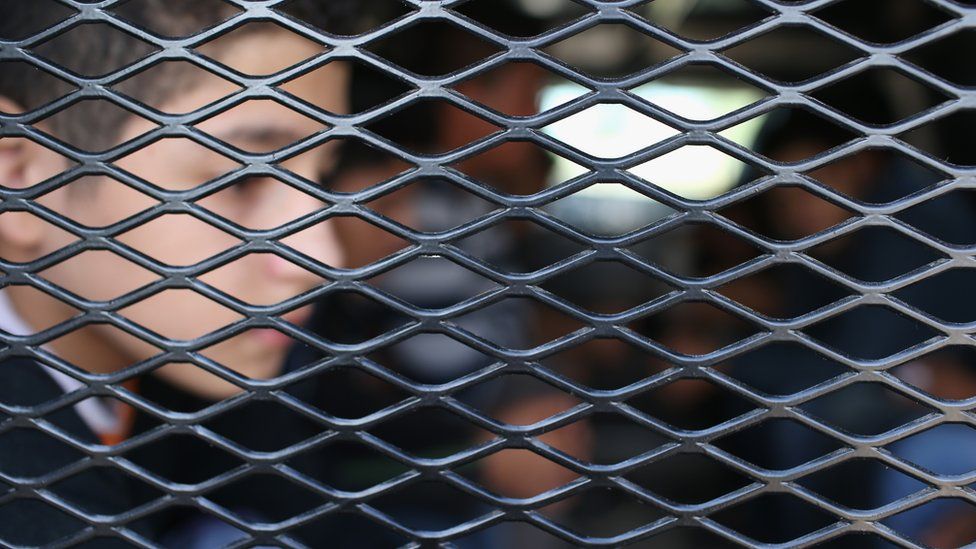 Boy behind a caged barrier in a detention vehicle