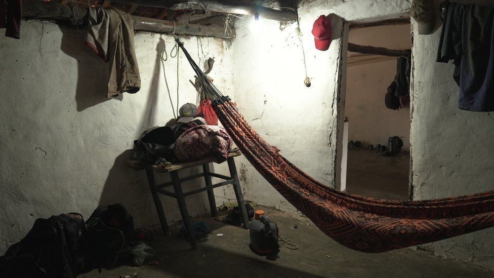 A hammock hangs in sparsely-lit basic living quarters