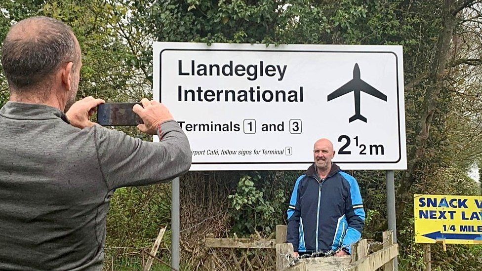 A man taking a photo of his friend outside the airport sign
