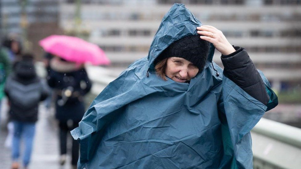 A person holds their hood up during heavy rain on Westminster Bridge