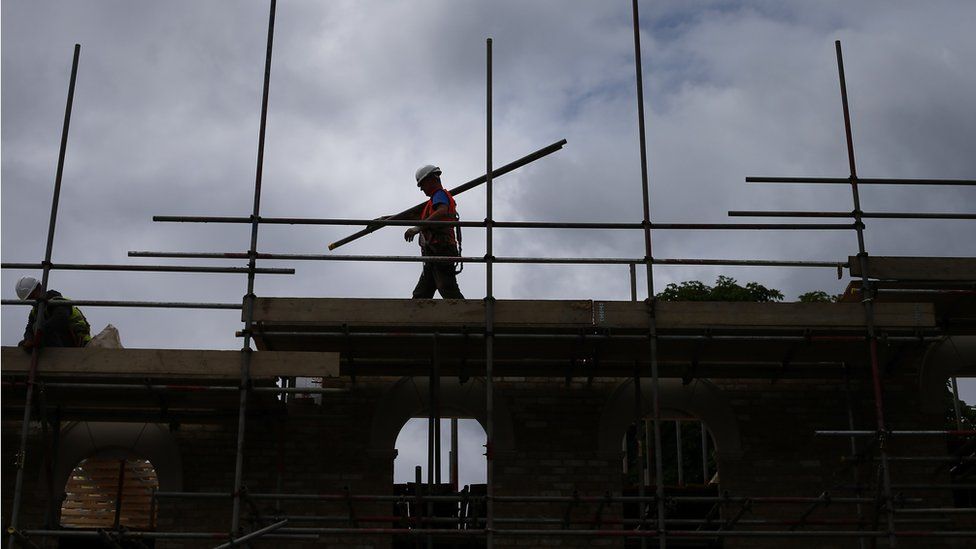 A builder assembles scaffolding as he works on new homes