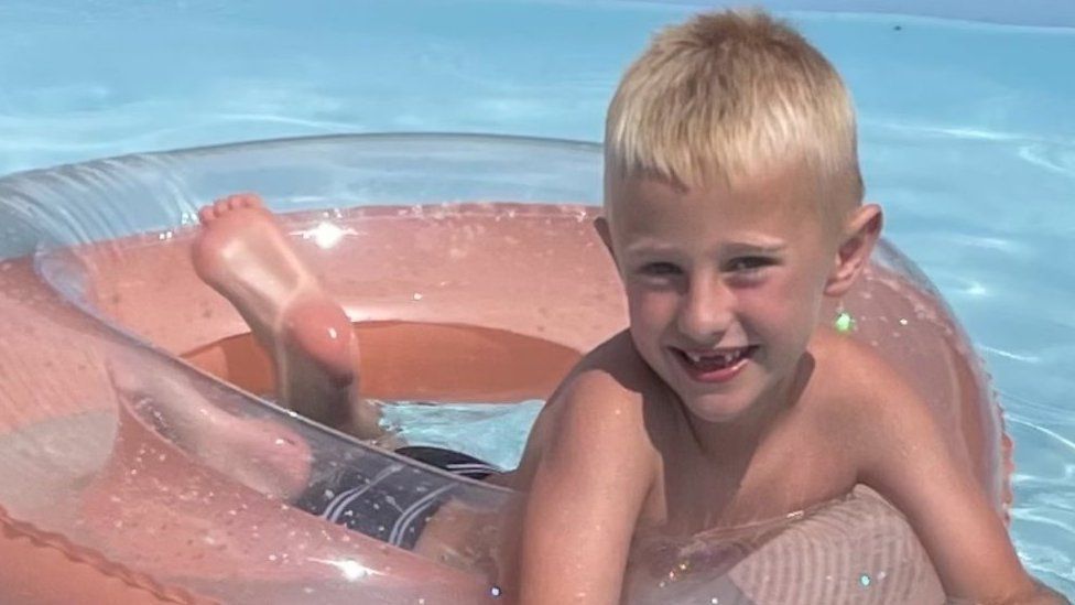 Freddie Farrow, who is blond, lying on an inflatable doughnut in a swimming pool.