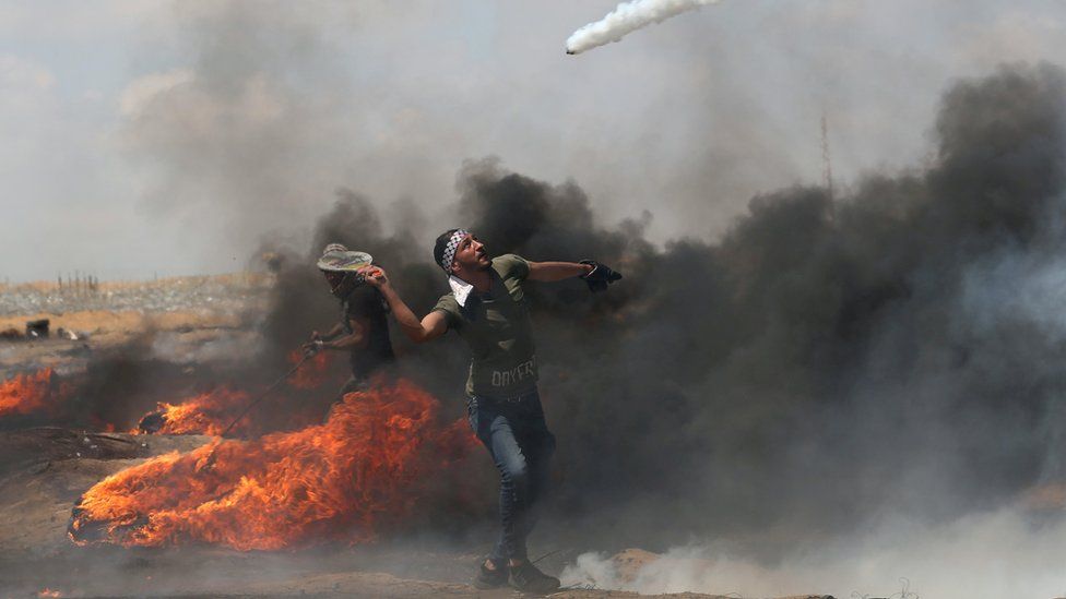 A Palestinian man uses a tennis racquet to return a tear-has canister fired by Israeli troops during a protest near the Gaza-Israel border fence (11 May 2018)