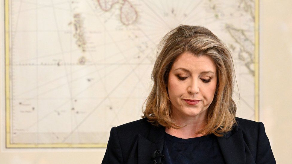 Penny Mordaunt stood at event next to map