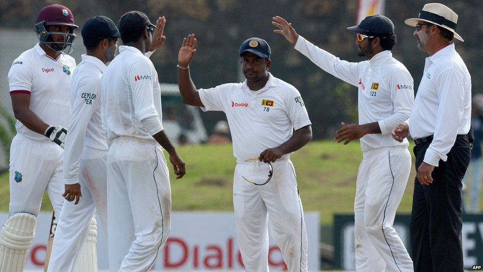 A file picture taken on October 16, 2015 shows Sri Lankan spinner Rangana Herath (C) being congratulated by teammates at the close of play of the West Indies" first innings during the third day of the opening