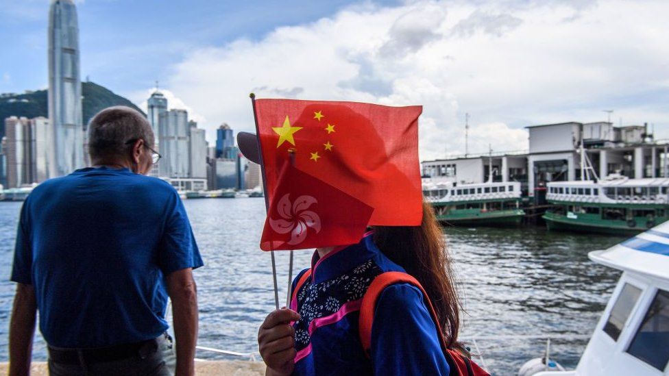 A woman carries the Chinese and Hong Kong flags while walking down Victoria Harbour in Hong Kong