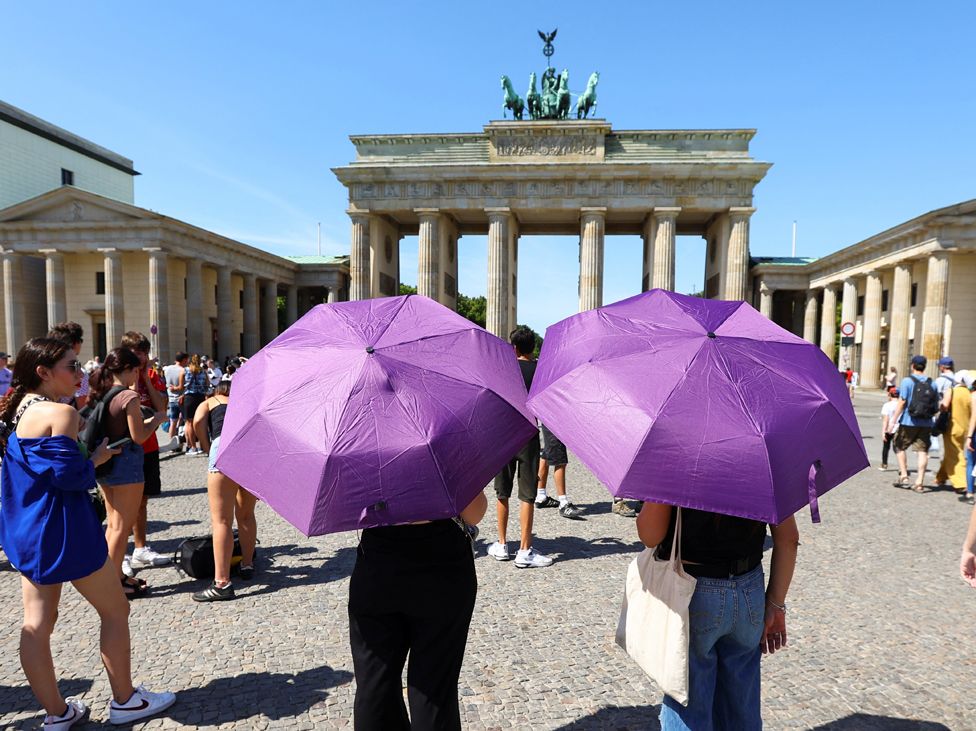 Женщины защищаются от солнца зонтиками во время жары перед Бранденбургскими воротами в Берлине, Германия,
