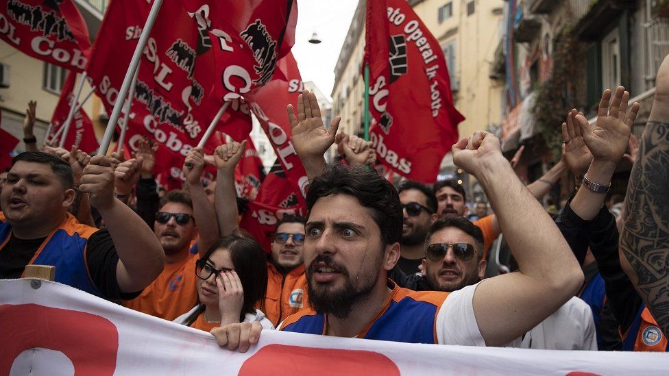 Workers hold banners and wave red flags as they take part in a demonstration to mark May Day in Naples, Italy.