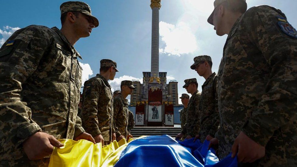 Украинские военные держат украинский флаг над гробом военнослужащего