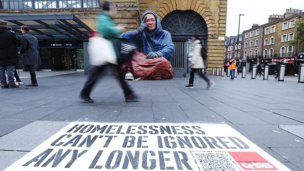 People walking by a a spray-painted message that says homelessness "can't be ignored".