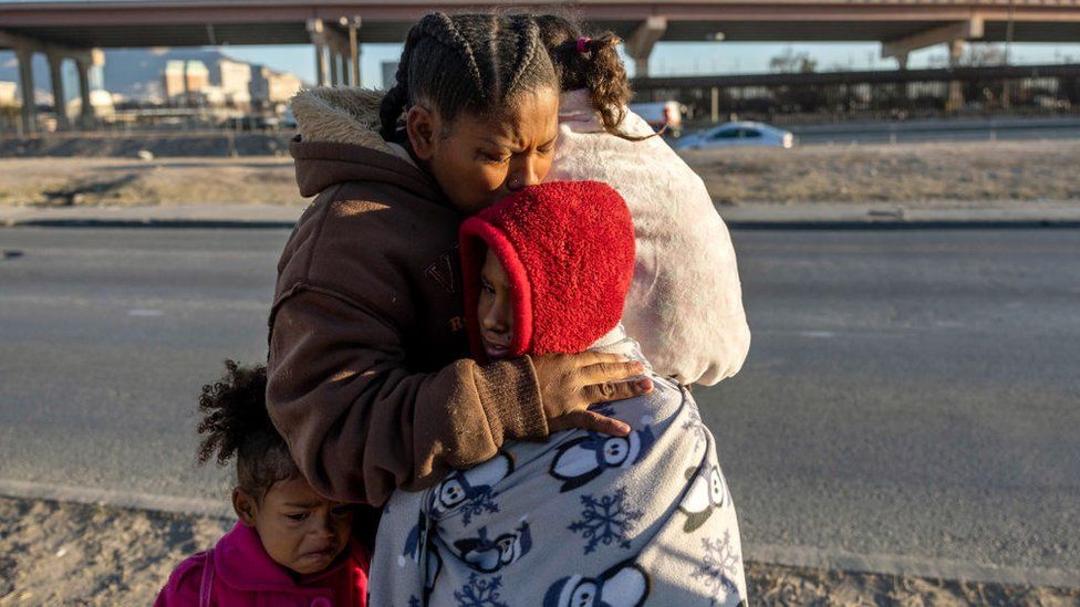 Венесуэльская иммигрантка Янейси Мартинес плачет, обнимая своих троих детей после того, как войска Национальной гвардии Техаса и полиция штата заблокировали популярный район пересечения границы 20 декабря 2022 года в Сьюдад-Хуаресе, Мексика