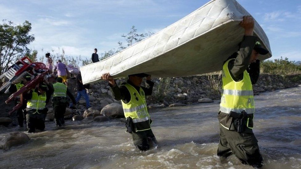 Colombian policemen carry a mattress as they help people to cross with their belongings to Colombia