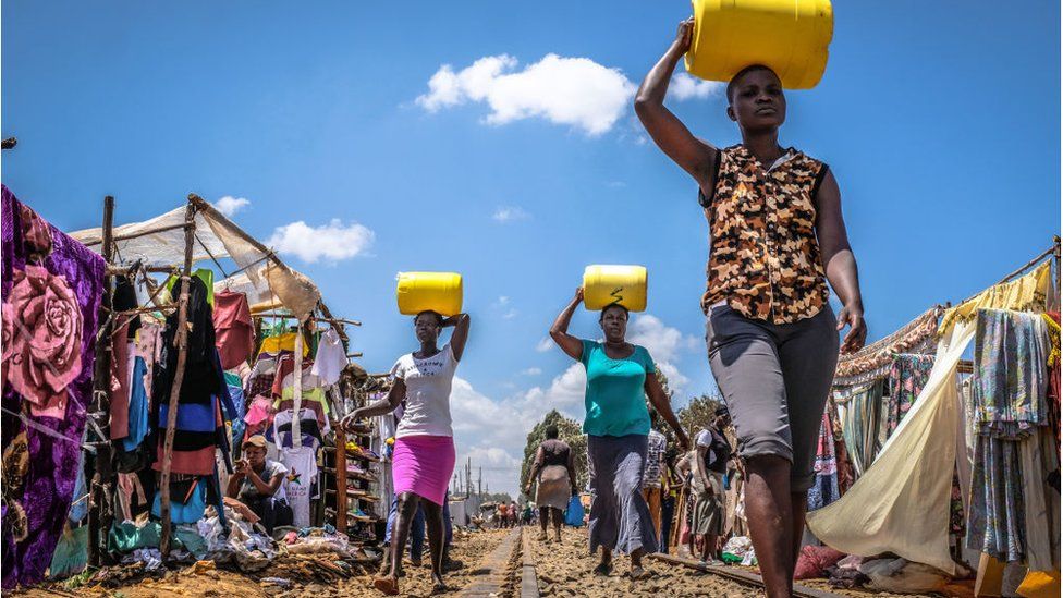 Women walk back home carrying water cans in Kibera