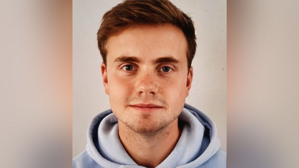 Photo of Jack who has brown hair, stubble, and is wearing a light blue hoodie.