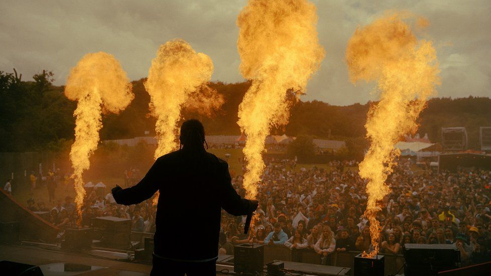 A performer stands on stage at Love Saves The Day in Bristol as flames shoot from the front of the stage
