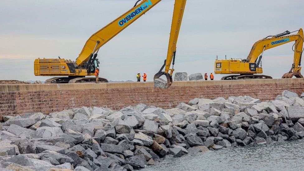 Two cranes lift the boulders alongside the port's sea defences