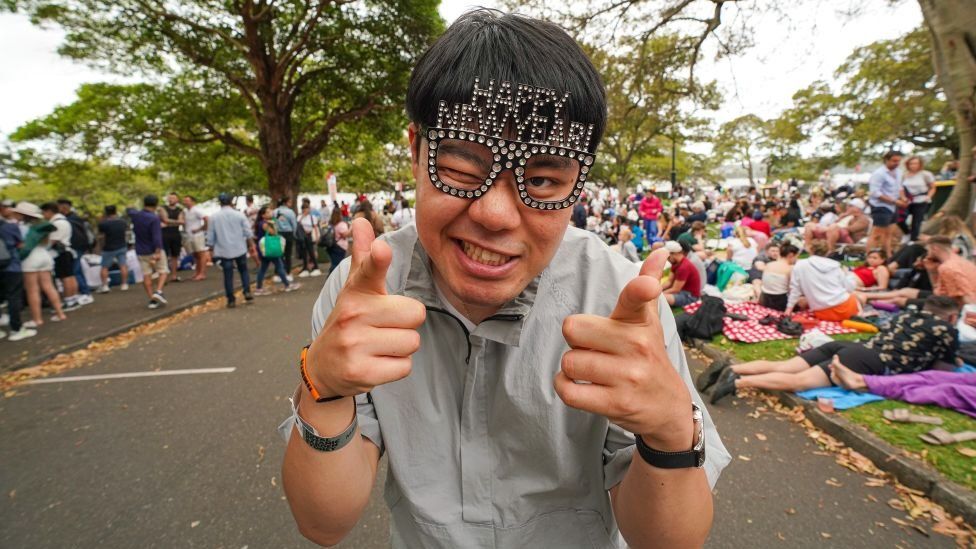 Man wears Happy New Year glasses and strikes a thumbs up as he celebrates New Year in Sydney