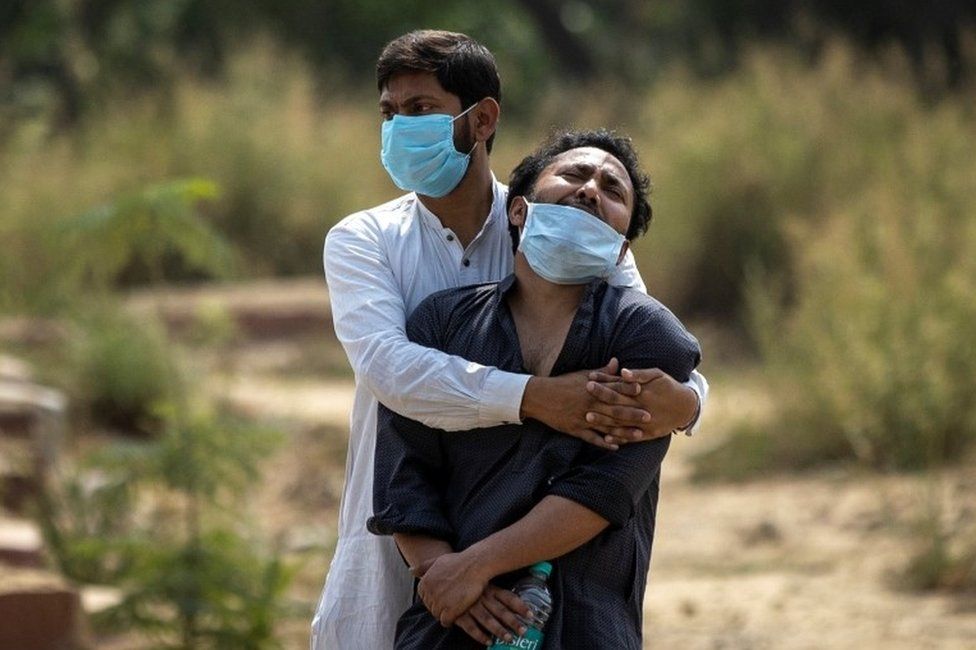 A man is consoled by his relative as he sees the body of his father, who died from the coronavirus disease (COVID-19), before his burial at a graveyard in New Delhi, India, April 16, 2021