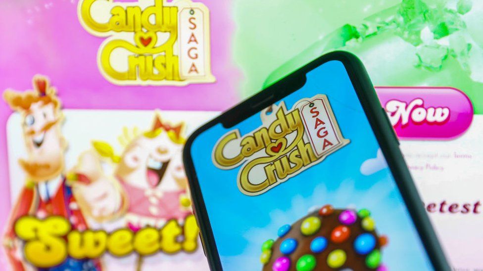 Candy Crush Saga logo displayed on a phone screen and Candy Crush website displayed in the background
