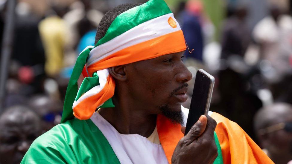 Ein Mann vor einem französischen Militärstützpunkt trägt während einer Protestaktion eine Niger-Flagge