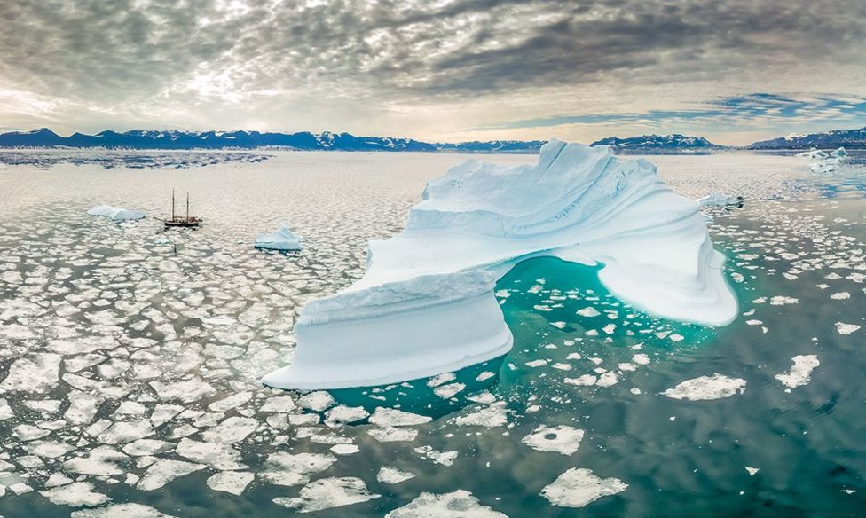An expanse of icy water with an iceberg and a ship