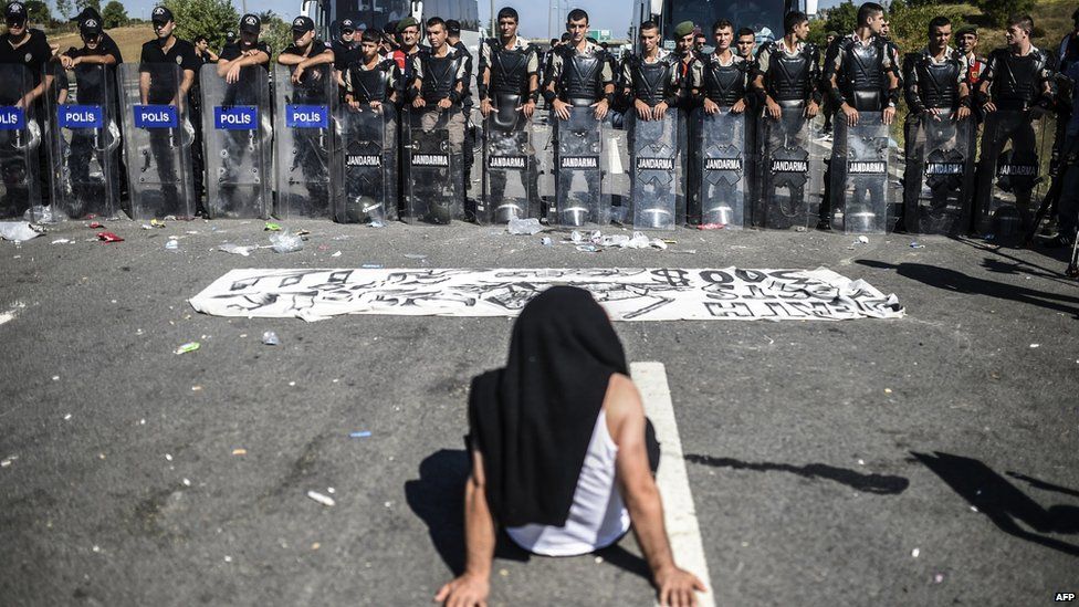 A man sits in front of Turkish police forces blocking migrants and refugees on a highway near Edirne as they march to the border between Turkey and Greece on 19 September 2015