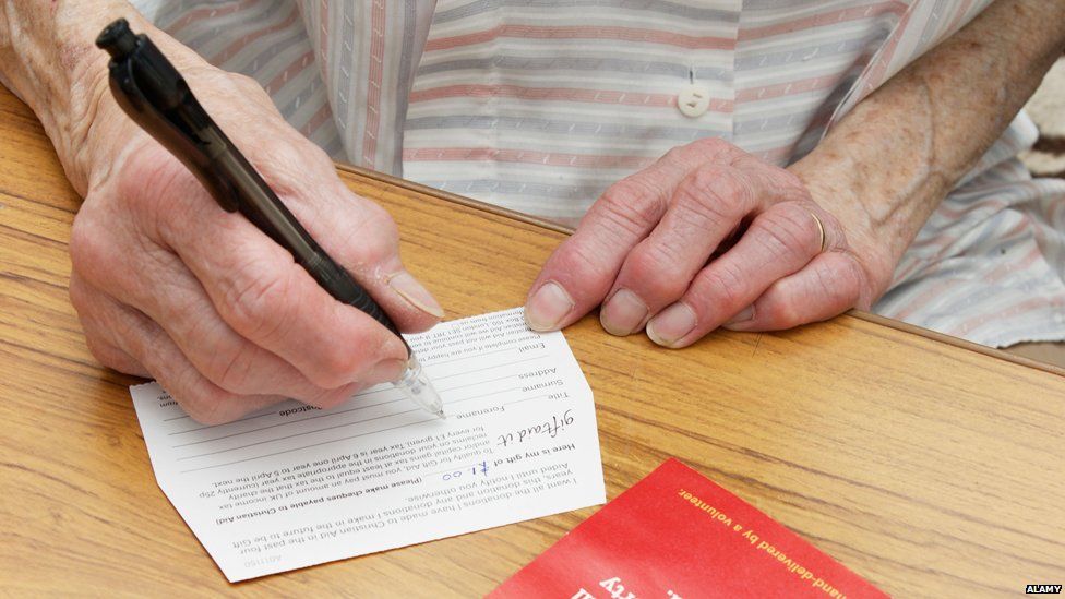 Elderly person writing on a giftaid envelope