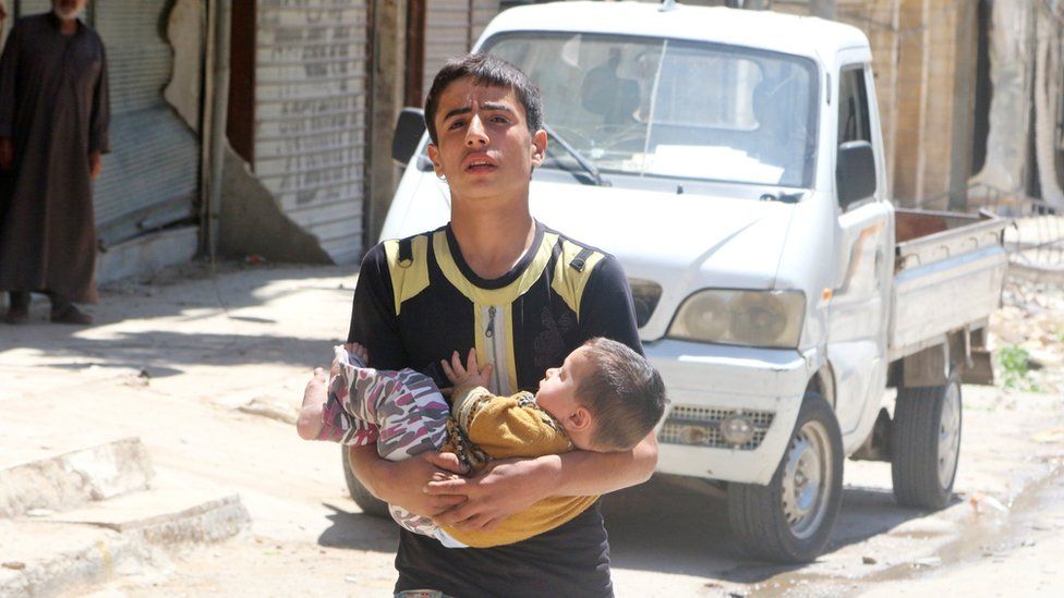 A boy carries a baby after a reported barrel bomb attack in the rebel-held Firdous district of Aleppo (29 April 2016)