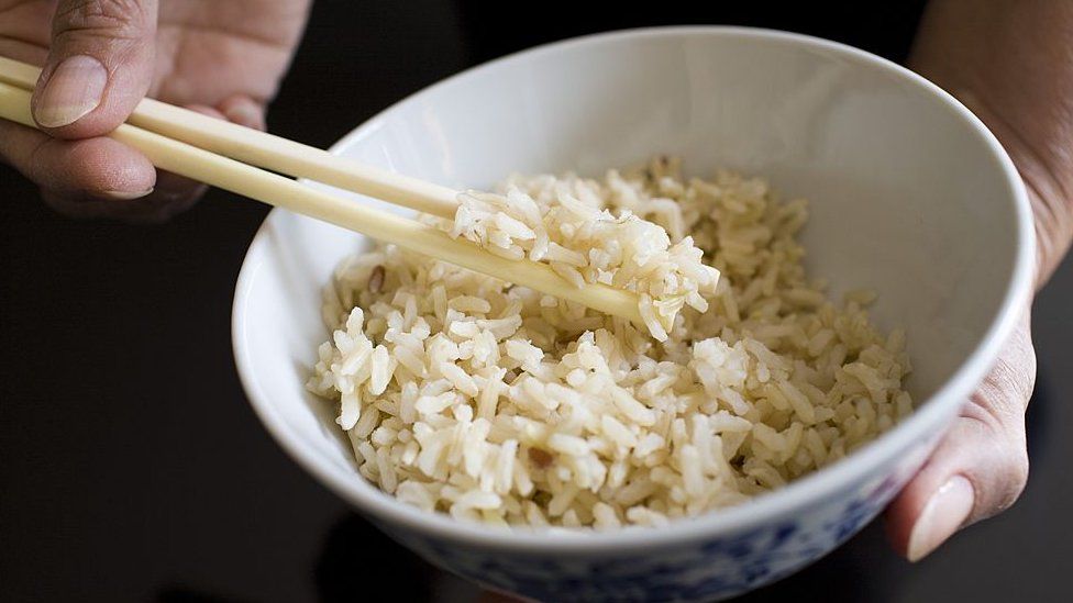 Asian woman holds bowl of brown wholegrain rice and chopsticks, Rice has become an expensive commodity as its in short supply,