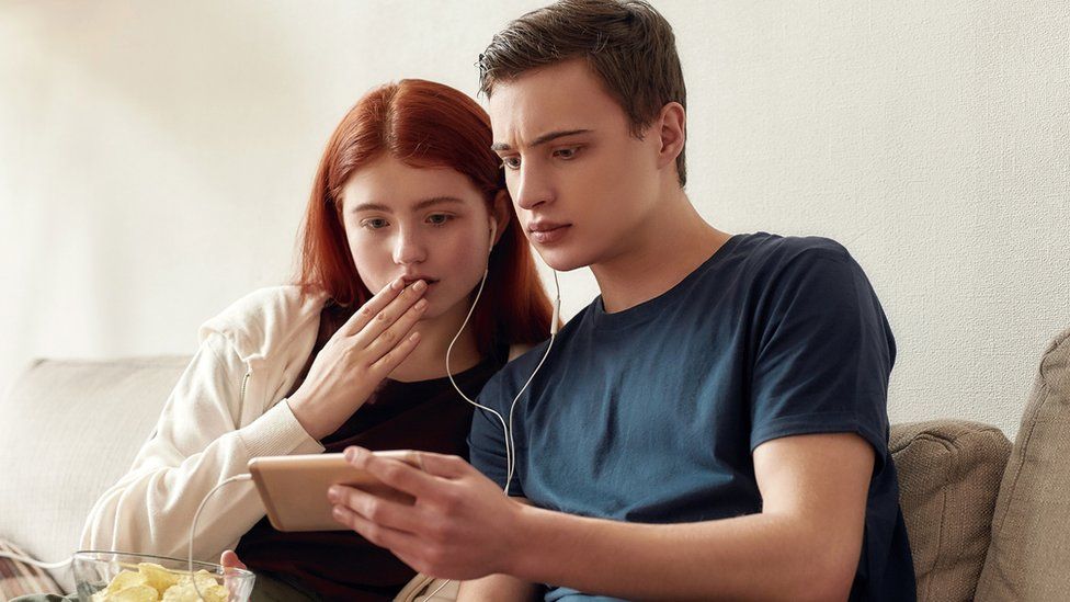 Stock image of teenagers looking worried watching a phone video