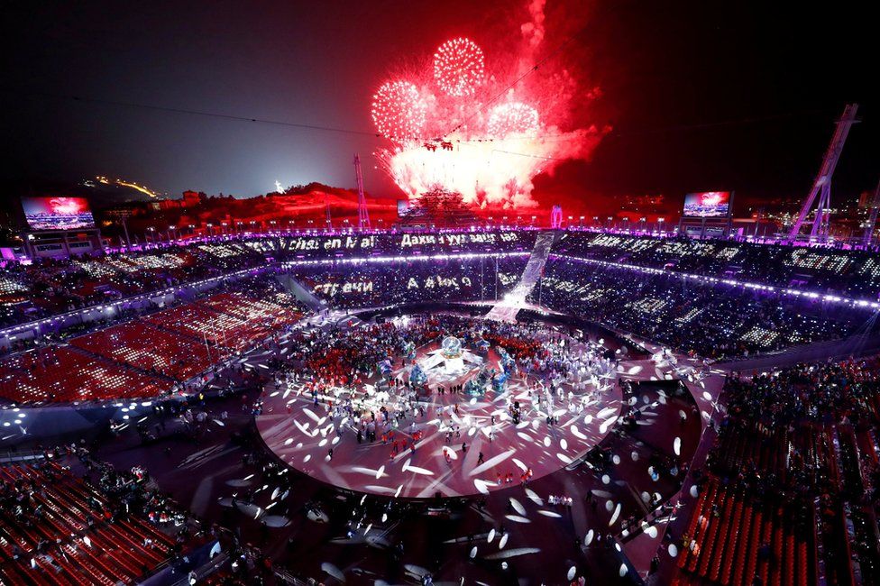 Red fireworks explore over a crowded Olympic stadium