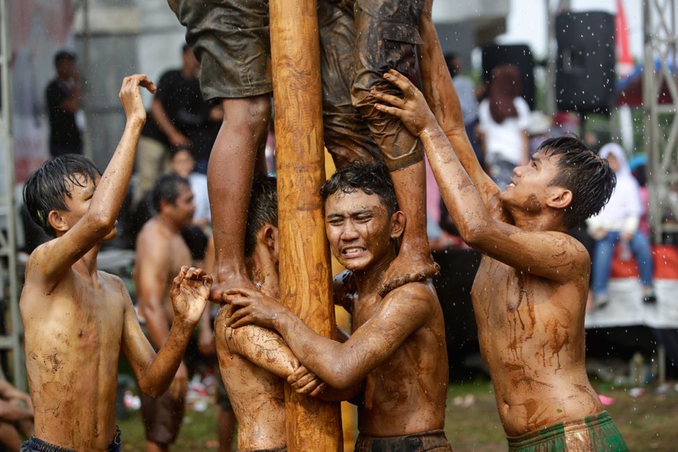 Indonesians take part in a palm tree climbing competition to reach prizes on top of the logs in Depok, Indonesia, on 17 August 2022
