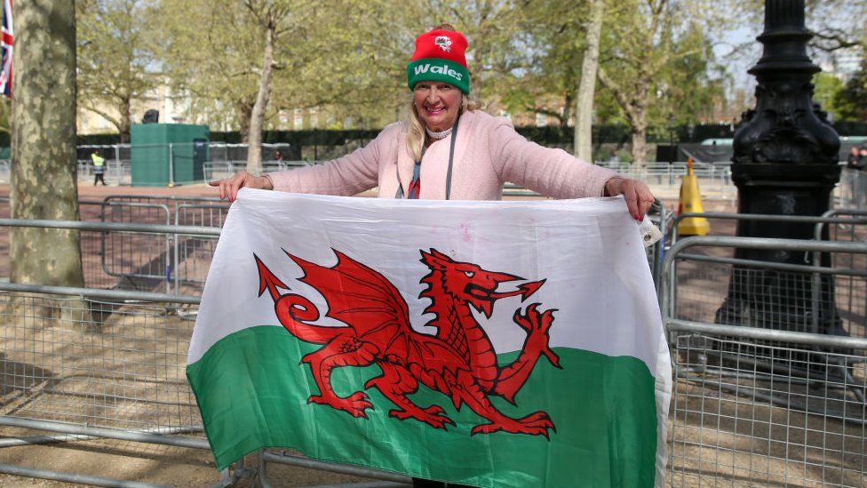 A royal fan holds aloft the Welsh flag outside Buckingham Palace