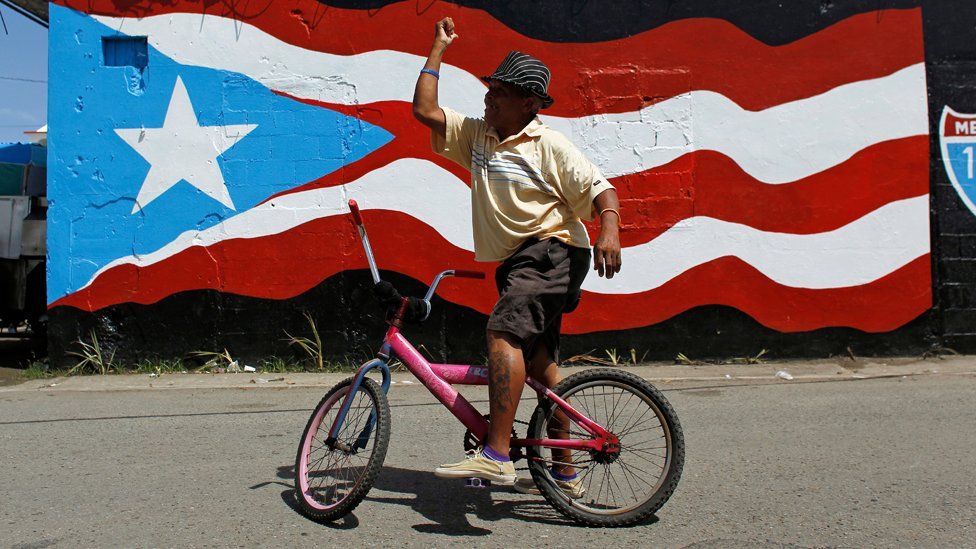 A man in front of a painting of a Puerto Rico flag