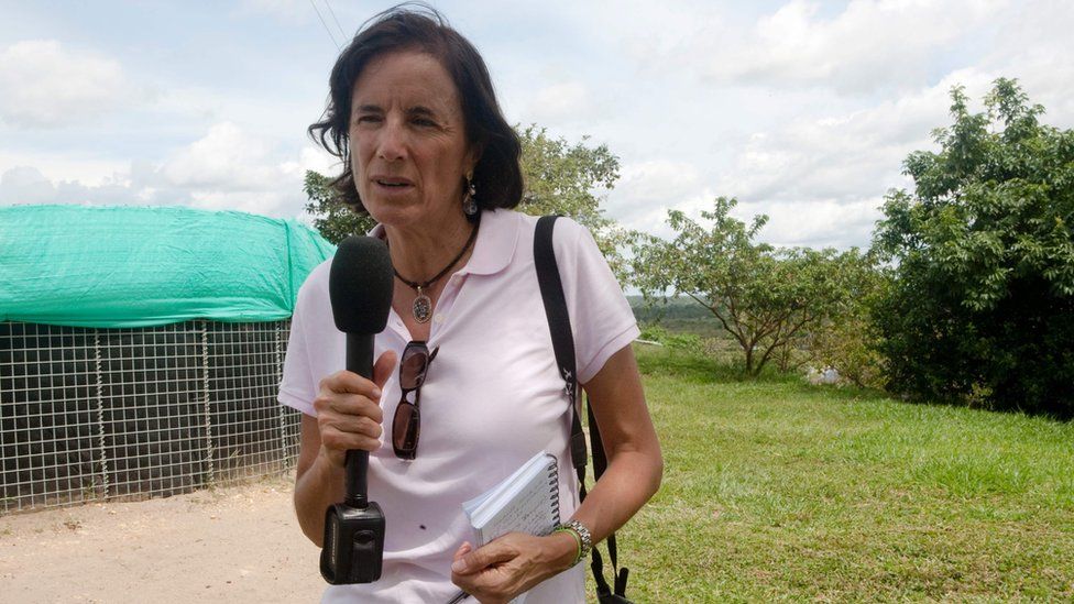 file picture of Salud Hernandez Mora outdoors, holding a microphone and a pen, and with a camera hanging from her wrist