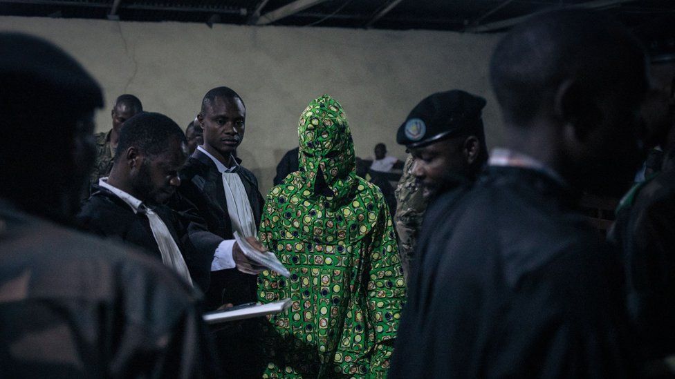 A masked witness leaves a court in Goma, DRC, during a trial against six soldiers accused of crimes against humanity.
