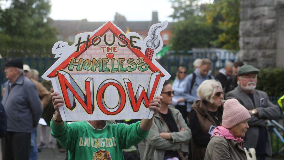 A protester holds a placard that reads: HOUSE THE HOMELESS NOW