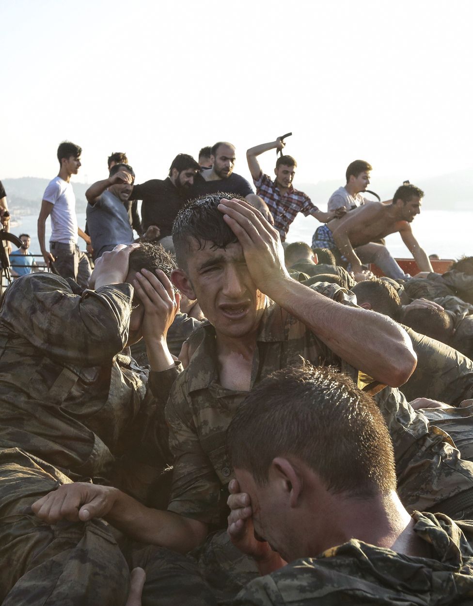 Civiles golpenado militares en el fondo de la foto y en el frente soldados jóvenes ocn el rostro en las manos en señal de desesperación