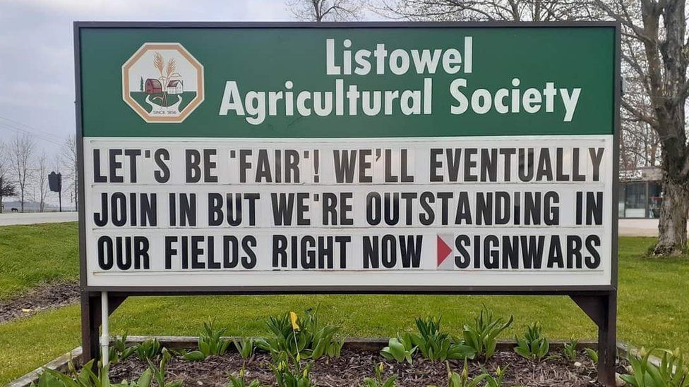 A sign from an agricultural company reads 'We'll eventually join in but we're out standing in our fields right now'